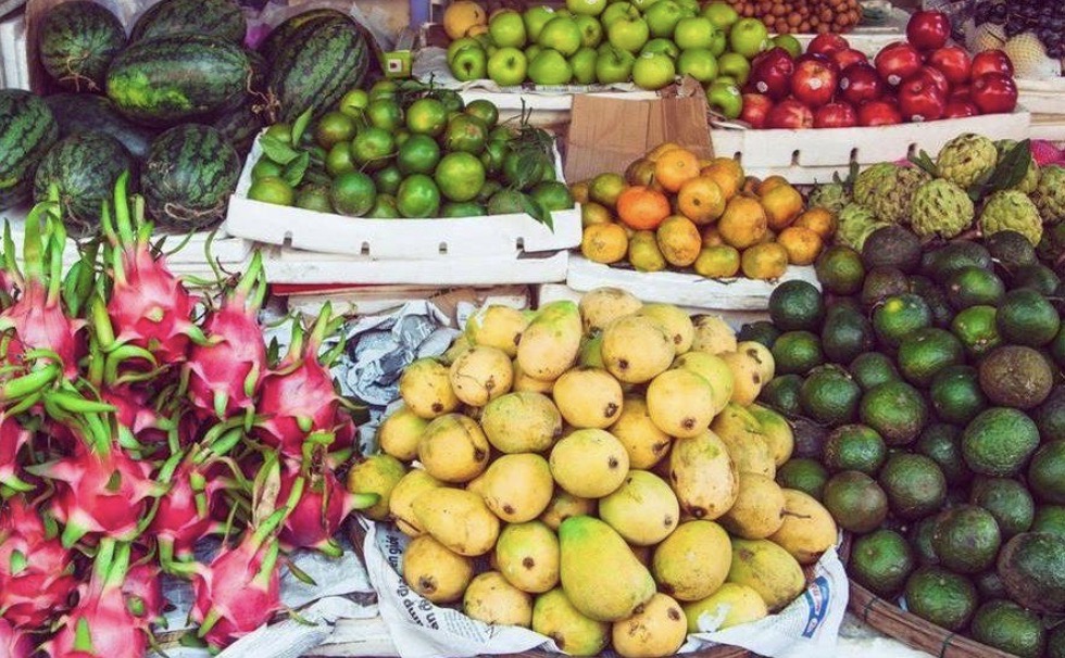 A vibrant display of fresh tropical fruits in a Vietnamese market including dragon fruit, mangoes, and avocados