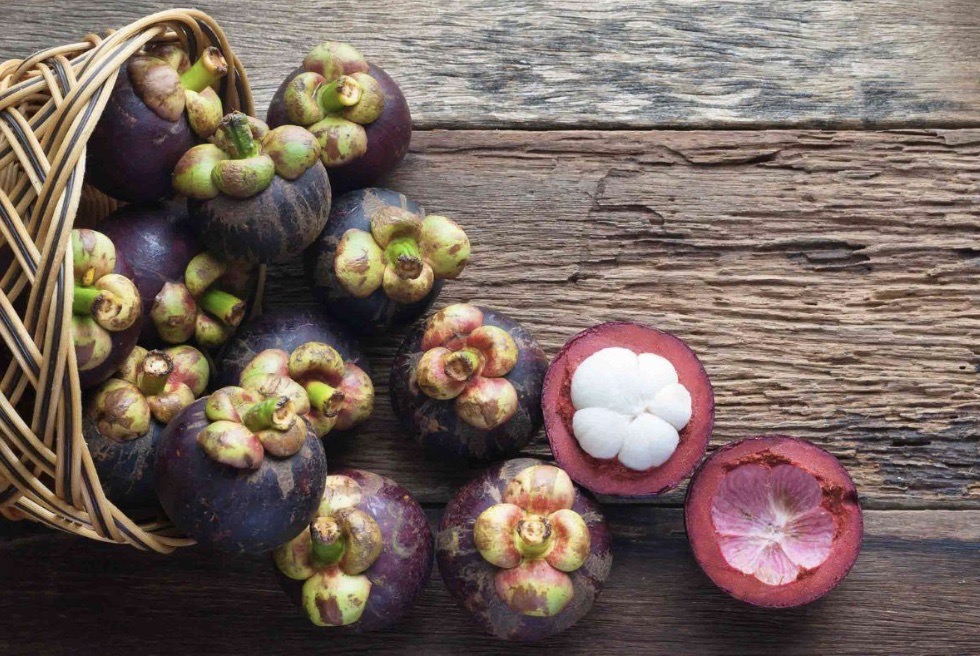 A rustic woven basket spilling fresh whole and half-cut mangosteens onto a wooden table